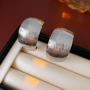 Macro shot of silver C-shaped earrings with brushed metal texture in a luxury jewelry box