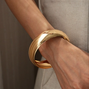 Detailed close-up of a wide polished gold metal cuff bracelet on a model's wrist