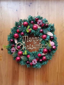 Close-up of a Christmas wreath featuring pine needles, red baubles, and candy ornaments