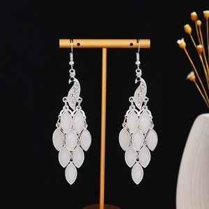 Detailed close-up of peacock-shaped silver earrings with white teardrop stones on a black background