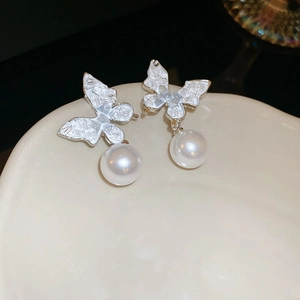 Macro detail of butterfly earrings with silver edging and a glossy white pearl drop