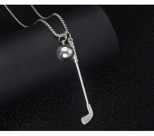 Detailed view of silver golf club and ball pendant necklace on a dark textured background