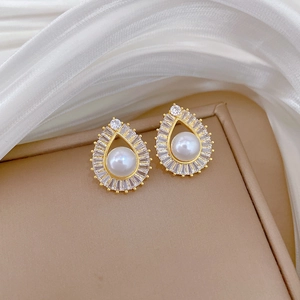 Detail view of teardrop gold earrings with central pearl and zircon halo on beige tray