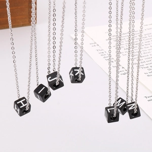 Détail montrant divers pendentifs alphabets cubes noirs de H à N sur chaînes argentées