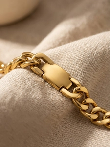 Macro detail of high-polish gold Cuban link bracelet with rectangle buckle on beige fabric