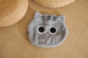 Dettaglio del morbido cuscino gatto in peluche grigio con grandi occhi ricamati su legno