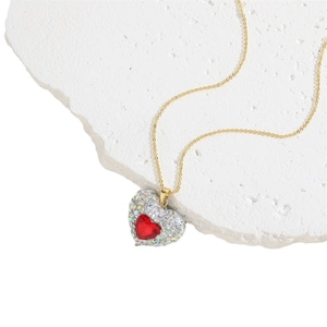 Golden heart necklace with red gemstone and micro-pave zirconia on a white stone background