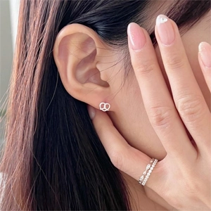 Detail of silver knot stud earrings and stacked crystal rings on a female model