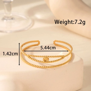 Minimalist gold triple-layer beaded open cuff bracelet on a white stone display pedestal