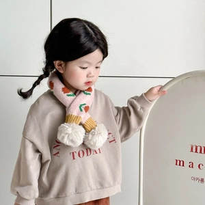 Close-up of pink knit scarf with strawberry pattern and soft beige pom-poms for children