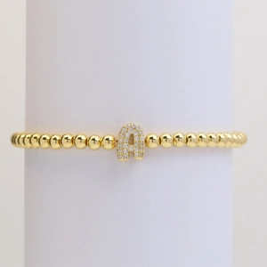 Close-up of golden beaded elastic bracelet with a sparkling zircon letter A charm