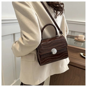 Detail view of dark brown faux crocodile leather handbag with silver round buckle