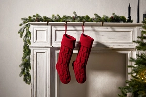 Pair of red cable knit Christmas stockings hanging on a white mantel with pine branches