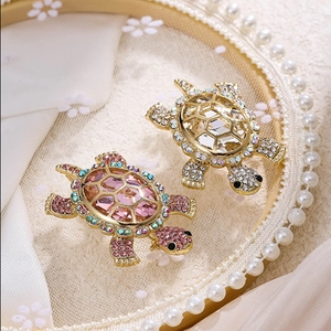 Detailed close-up of golden turtle brooches with pink crystals and shimmering rhinestones