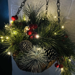 Gros plan d'un panier de Noël suspendu avec aiguilles de pin, baies rouges et lumières LED