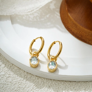 Macro shot of 18K gold hoop earring featuring an oval cubic zirconia stone with bezel setting