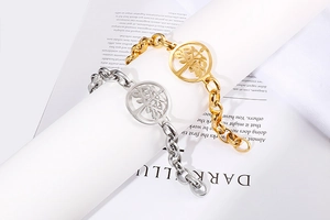 Dettaglio di bracciali a catena oro e argento con ciondoli albero della vita traforati