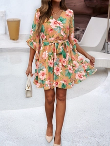 Detail of peach floral wrap dress with V-neckline, waist tie, and ruffled hem finish