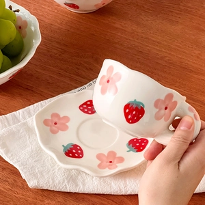 Close-up of hand-painted ceramic cup and wavy saucer with strawberry and flower motifs