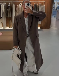 Detailed view of women's long brown wool coat paired with white wide-leg trousers