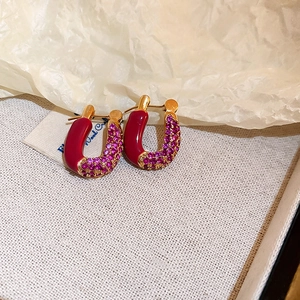 Detailed macro of U-shaped gold hoop earrings featuring red enamel and purple crystals