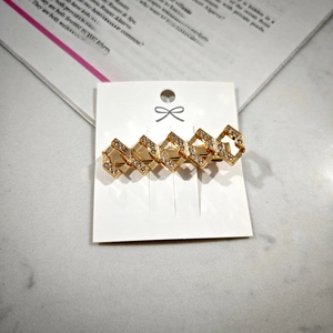 Detailed view of a gold alloy hair clip with crisscross diamond shape and small rhinestones