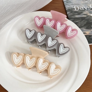 Three macaron jelly heart hair claws in pink, grey and beige on a ceramic plate
