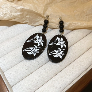 Close-up of black oval drop earrings with white lily floral patterns on jewelry tray