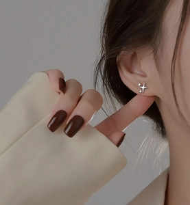Close-up of asymmetrical silver four-pointed star earrings worn on a model's ear