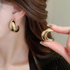 Détail de boucles d'oreilles dorées en forme de C portées par un mannequin