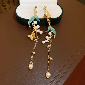 Detailed view of crane drop earrings with teal enamel leaf and white lily of the valley buds
