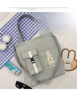 Close-up of light gray canvas tote bag featuring NICE letter print and buckle pocket detail