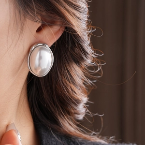 Close-up of French vintage oval pearl earrings with silver textured edges on model
