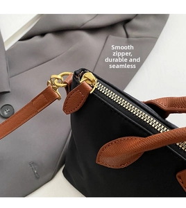 Detail of smooth gold zipper and brown leather handle on a black nylon tote bag