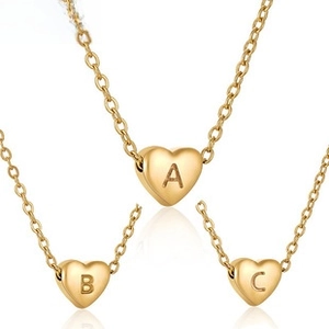 Detail of gold heart pendant necklaces featuring engraved initials A, B, and C in macro view