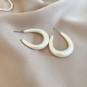 Close-up of pearlescent cream U-shape acrylic hoop earrings on elegant silk background