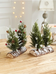 Close-up of mini snow-covered Christmas trees with natural wood bases and red berries
