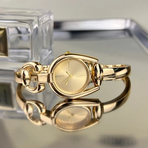 Macro detail of golden horseshoe-shaped bangle watch with elegant Roman numerals