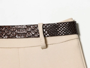 Détail d'une ceinture marron texture serpent sur un pantalon en sergé beige de style décontracté