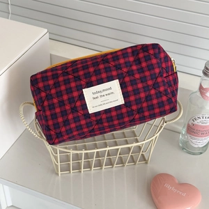 Detail of red and blue plaid quilted cosmetic bag with yellow zipper in a white basket