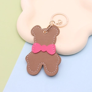 Detail of a brown leather-texture bear keychain with a pink bow and golden metal ring