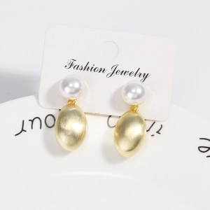 Close-up of pearl stud earrings with brushed gold metal teardrop pendants on card