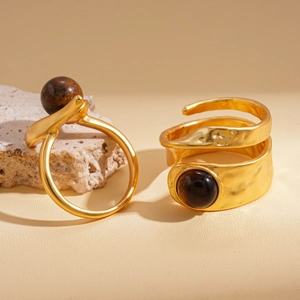 Two golden open rings with tiger eye stone set on a minimalist warm beige stone pedestal