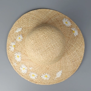 Top view of woven sun hat featuring delicate white daisy embroidery on natural straw material