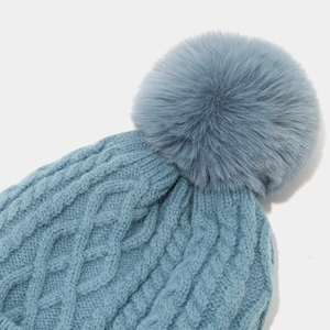 Detailaufnahme der blauen Strickmütze mit Rautenmuster und flauschigem Kunstfell-Bommel