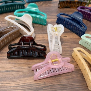 Assorted colorful large 10cm perfume bottle hair claws displayed on a dark wood table
