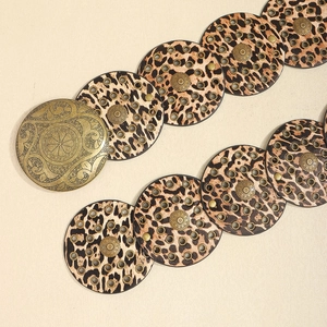 Macro detail of a vintage leopard print belt with round links and bronze metal buckle