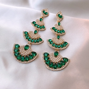 Macro shot of tiered fan-shaped gold earrings with green pear-cut gems on silk fabric