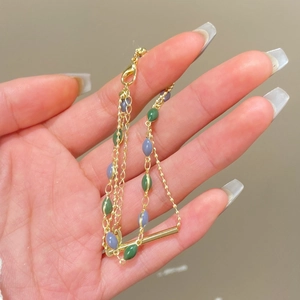 Dettaglio di un bracciale dorato a doppio strato con perle ovali verdi e viola vintage