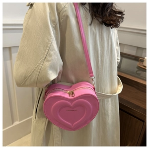 Detail of pink heart-shaped crossbody bag featuring fashion & bag text and metal zipper